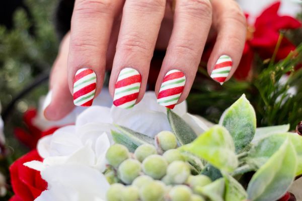 Unghie natalizie con base bianca e strisce diagonali rosse e verdi in stile caramella di Natale