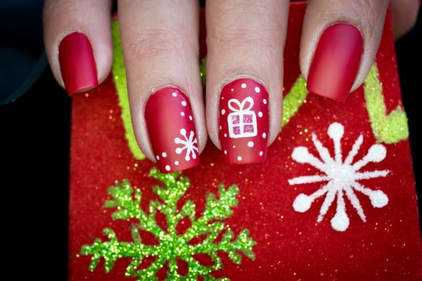 Unghie natalizie semplici con smalto rosso opaco, fiocchi di neve bianchi e disegno di un pacchetto regalo